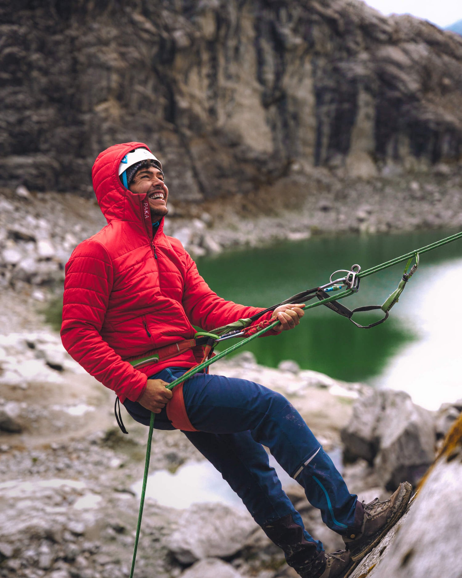 Man smiling while repelling from mountain in red winter jacket