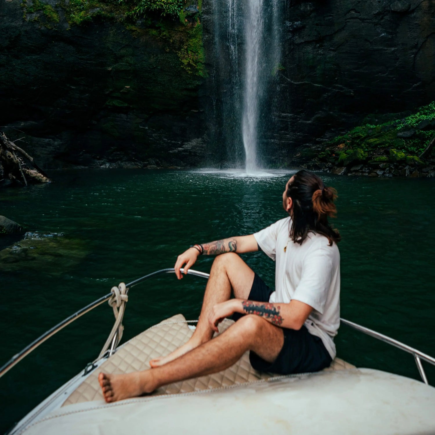 A man in a boat wearing a cream alpaca tee in front of a beautiful waterfall and lake 