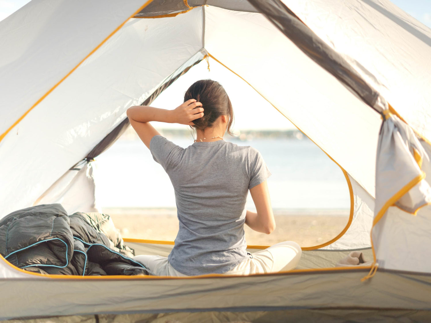 A  woman touching her hair in a camping tent, wearing a blue alpaca tee