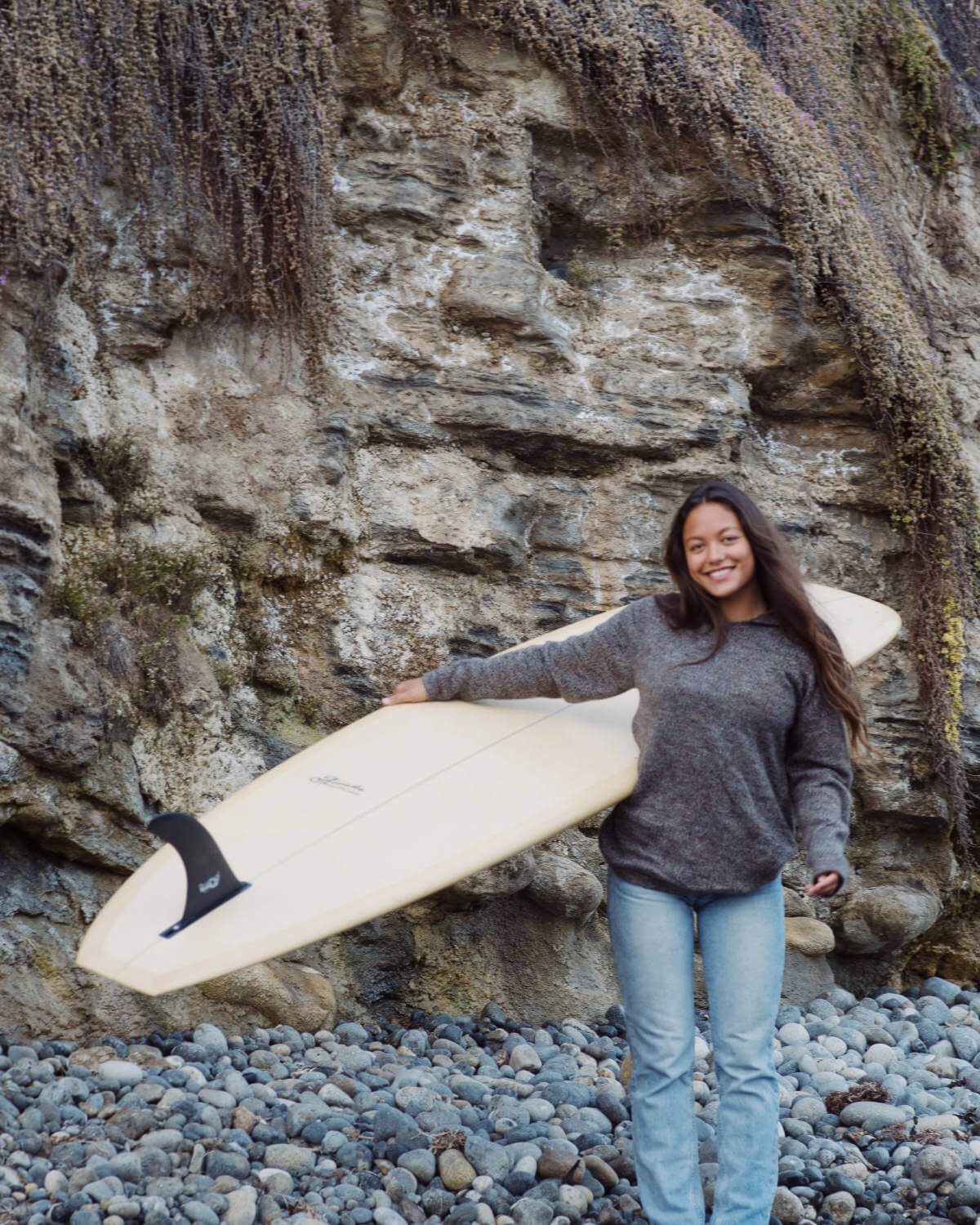 A smiling girl holding a surfboard in her Vida Hoodie