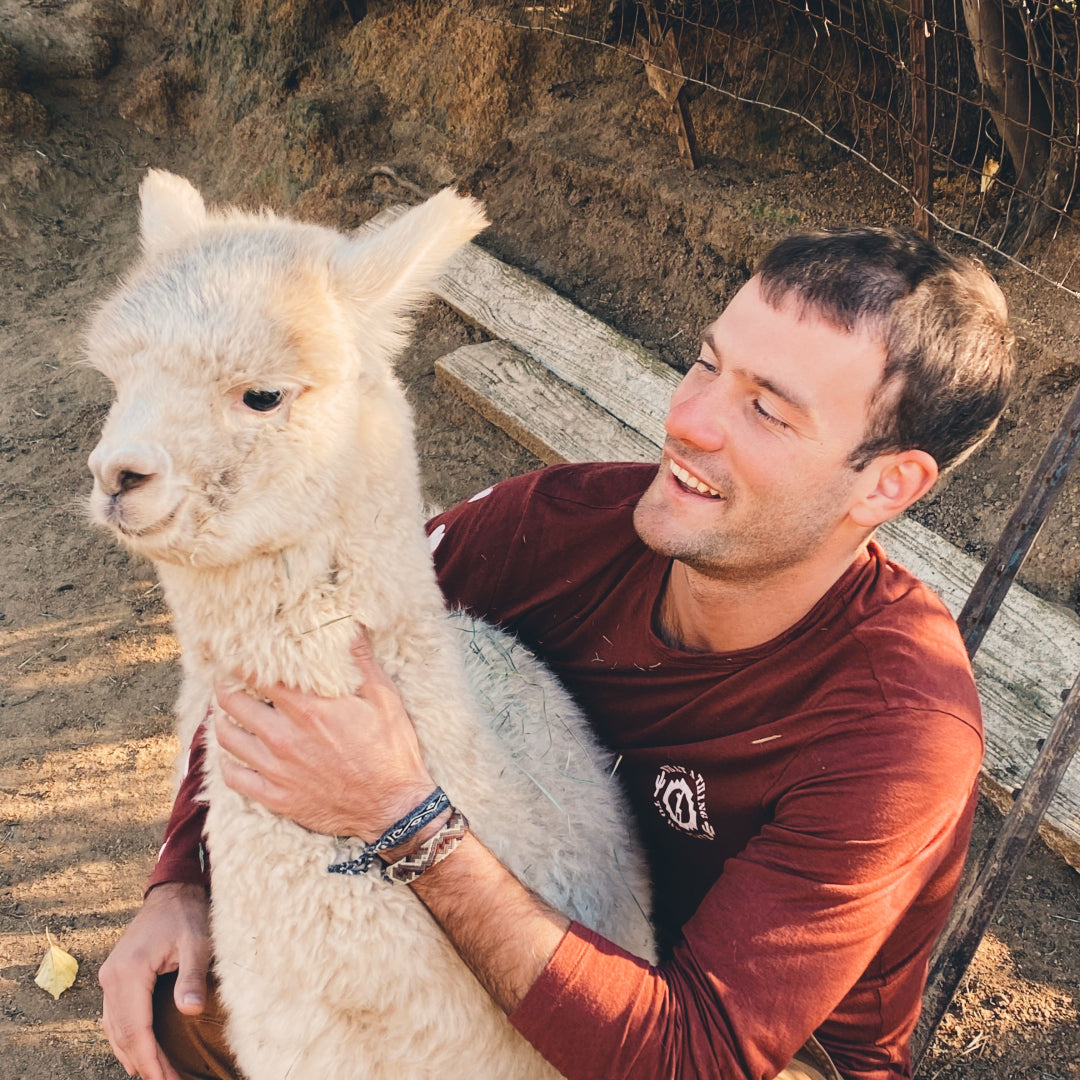 Kris Cody, our founder, petting a white alpaca in his clay Sebastian Baselayer
