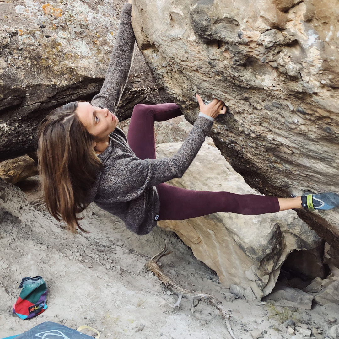 A woman climbing rocks in her Vida Hoodie