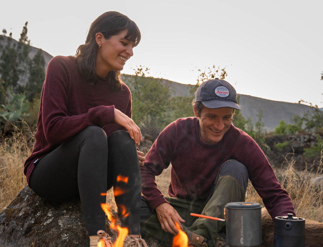 A couple at a campfire wearing their Cusco sweaters
