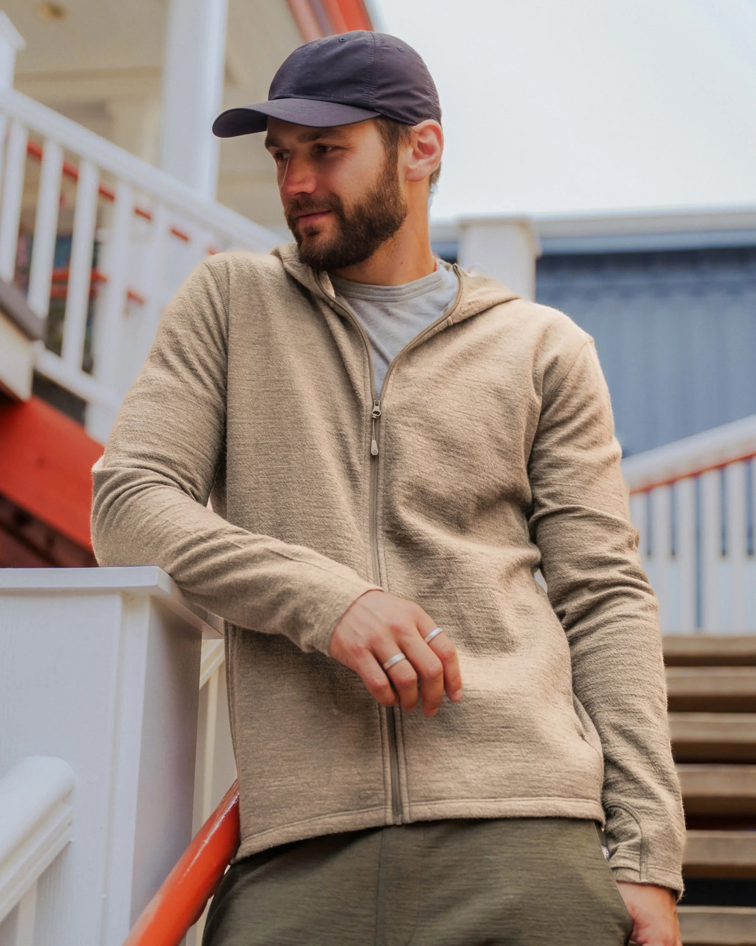 Three-quarter front of Men’s Breathe Full Zip Hoodie in timber showing slim athletic fit, hood, full zipper, and textured alpaca fabric on porch stairs
