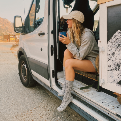 A beautiful woman sitting in a van, taking a cup of coffee in her Sebastian socks