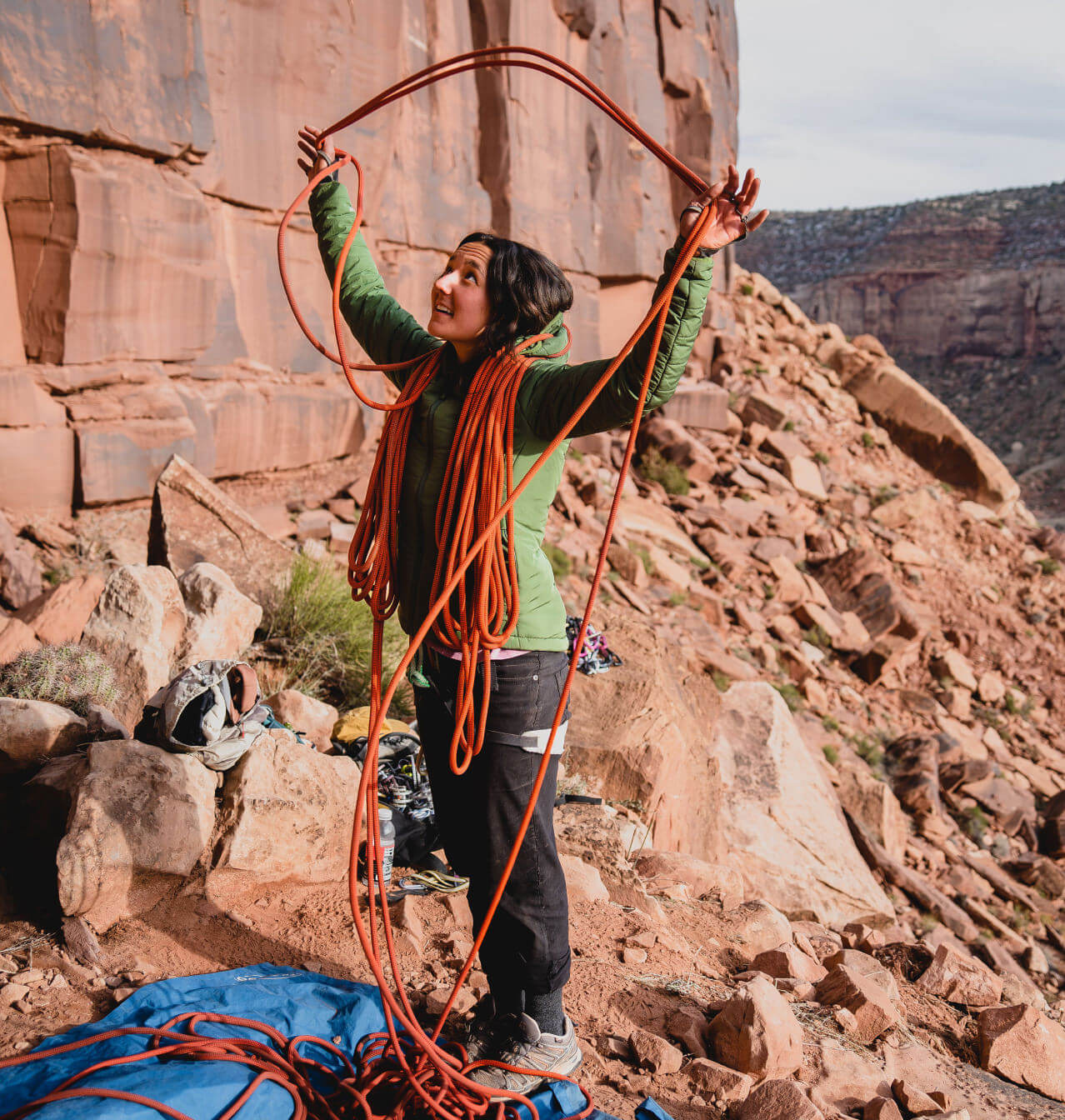 Climber in green jacket with orange rope about to climb in her gear
