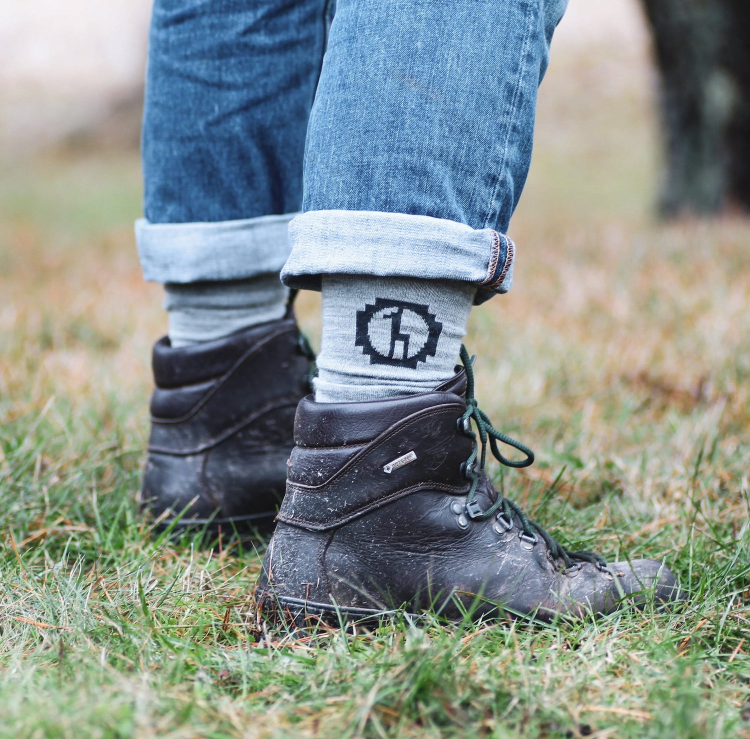 Photo of legs wearing jeans, light grey Paka socks, and leather boots outside on grass