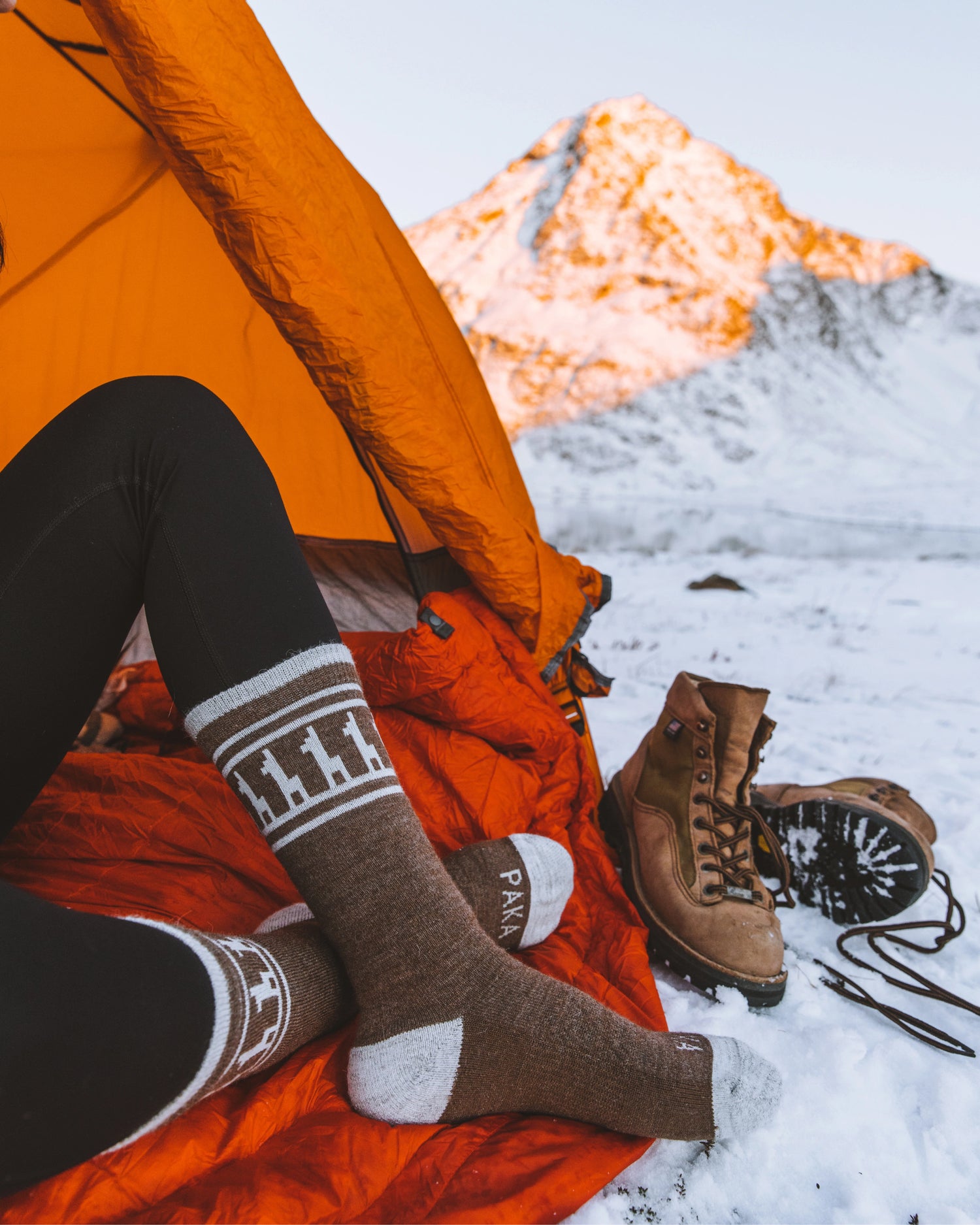 Side view of brown thermal crew socks on model showing alpaca motif and gray heel and toe in snowy campsite