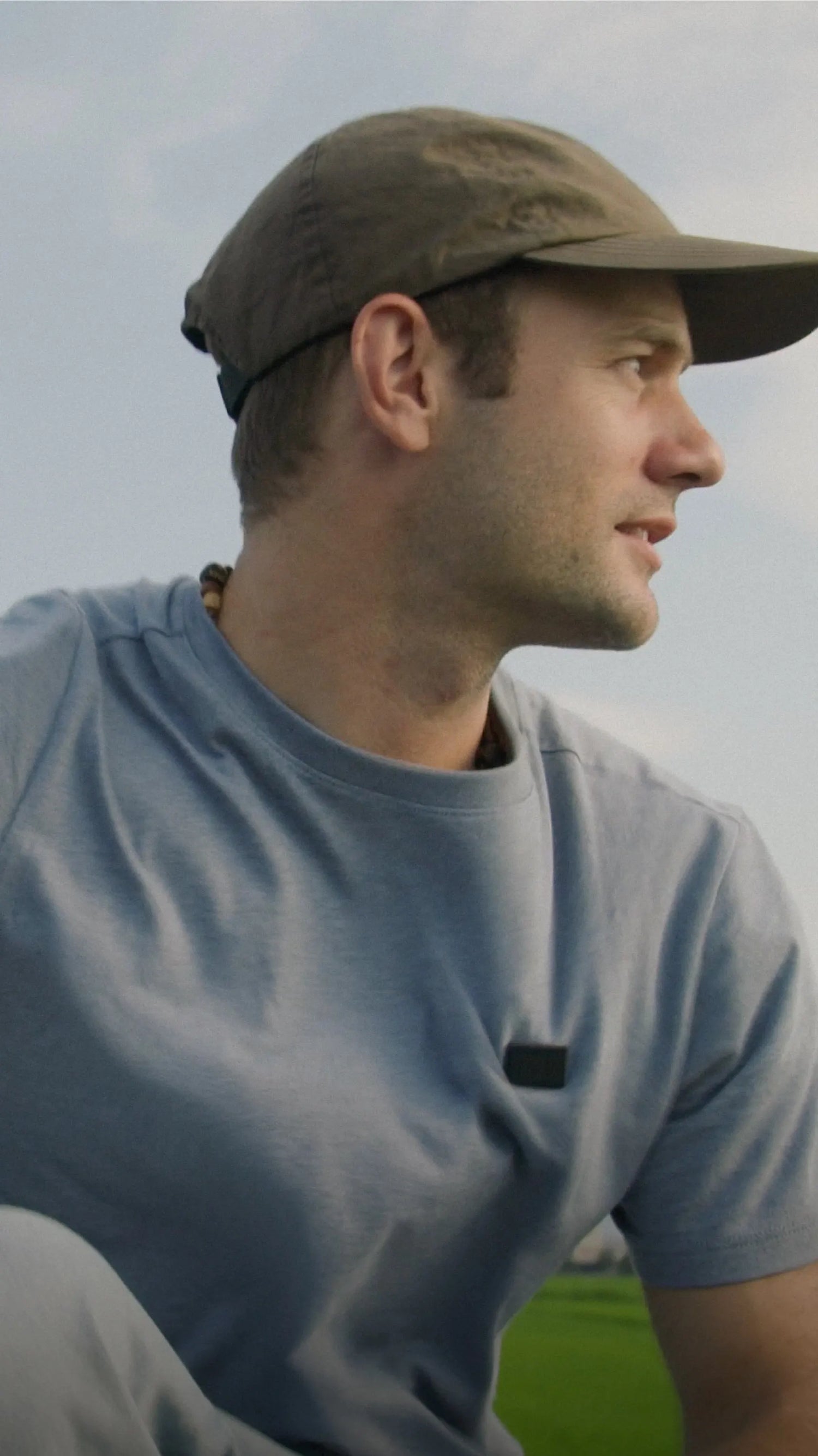 Man wearing a blue-gray T-shirt and cap outdoors in a natural setting