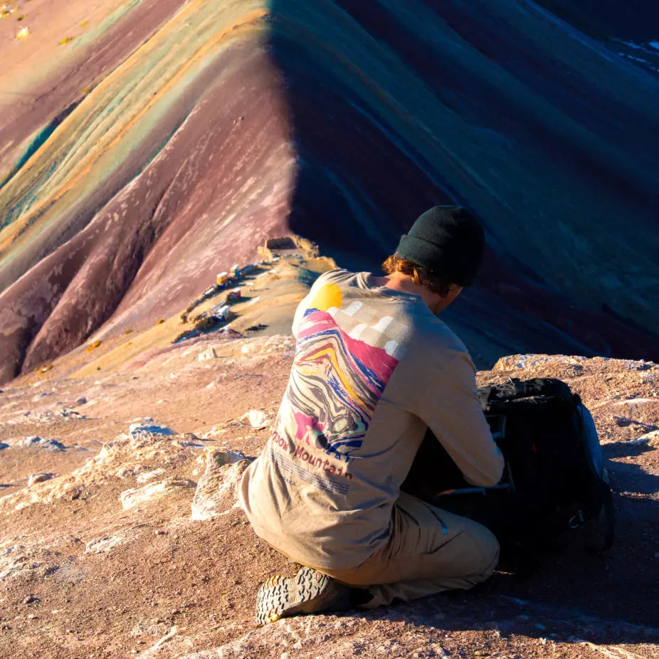 A man wearing his timber Long sleeve in front of the rainbow mountain. It is also printed at the back of the shirt