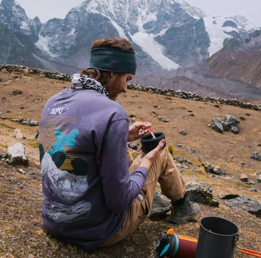 A man in his purple Explore Peru Long sleeve in the andes mountains preparing a tea