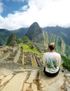 A Woman sitting in front of Machu Picchu wearing one of our Explore Peru long sleeves