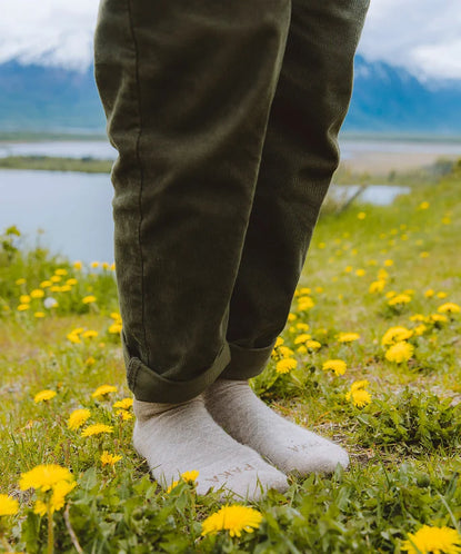 Person wearing white ankle socks standing on grass with yellow wildflowers by a lake and mountains