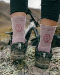 Back view of Trail 3/4 Crew socks in Quail showing mid-calf fit and logo on a model standing on rocky trail with bike