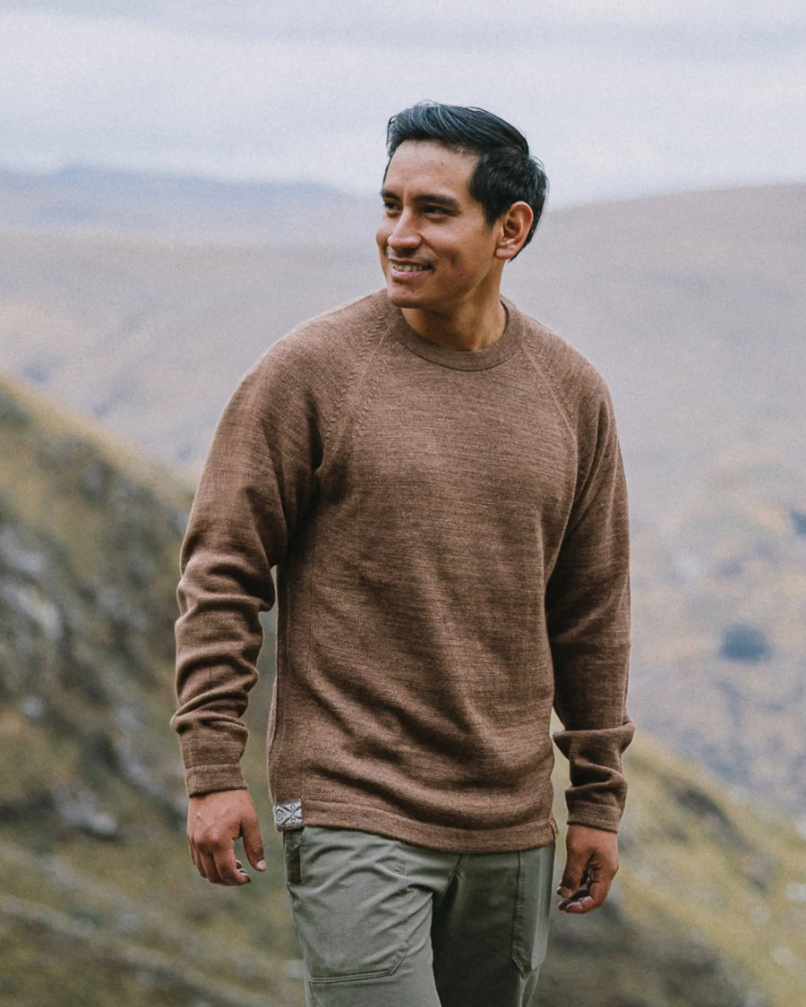 Man wearing a brown sweater standing in a mountainous landscape