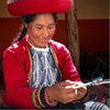 A smiling Quechua woman weaving alpaca fiber. She's wearing her traditional red dress