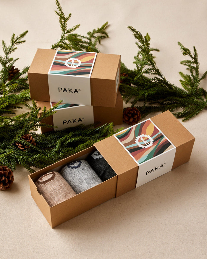 PAKA sock set in a cardboard box with decorative greenery on a neutral background