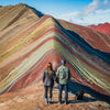 A couple standing in front of Rainbow mountain - a colorful mountain with reds, yellows, and greens.