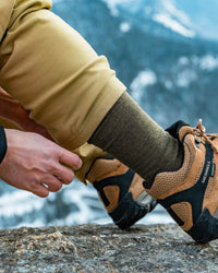 Side close-up of Essential Crew Socks in Andean Moss showing mid-calf alpaca knit and ribbed texture with hiking boot and mountain background