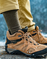 Person wearing dark moss green alpaca crew socks pulled up, paired with brown hiking boots on a snowy rocky trail