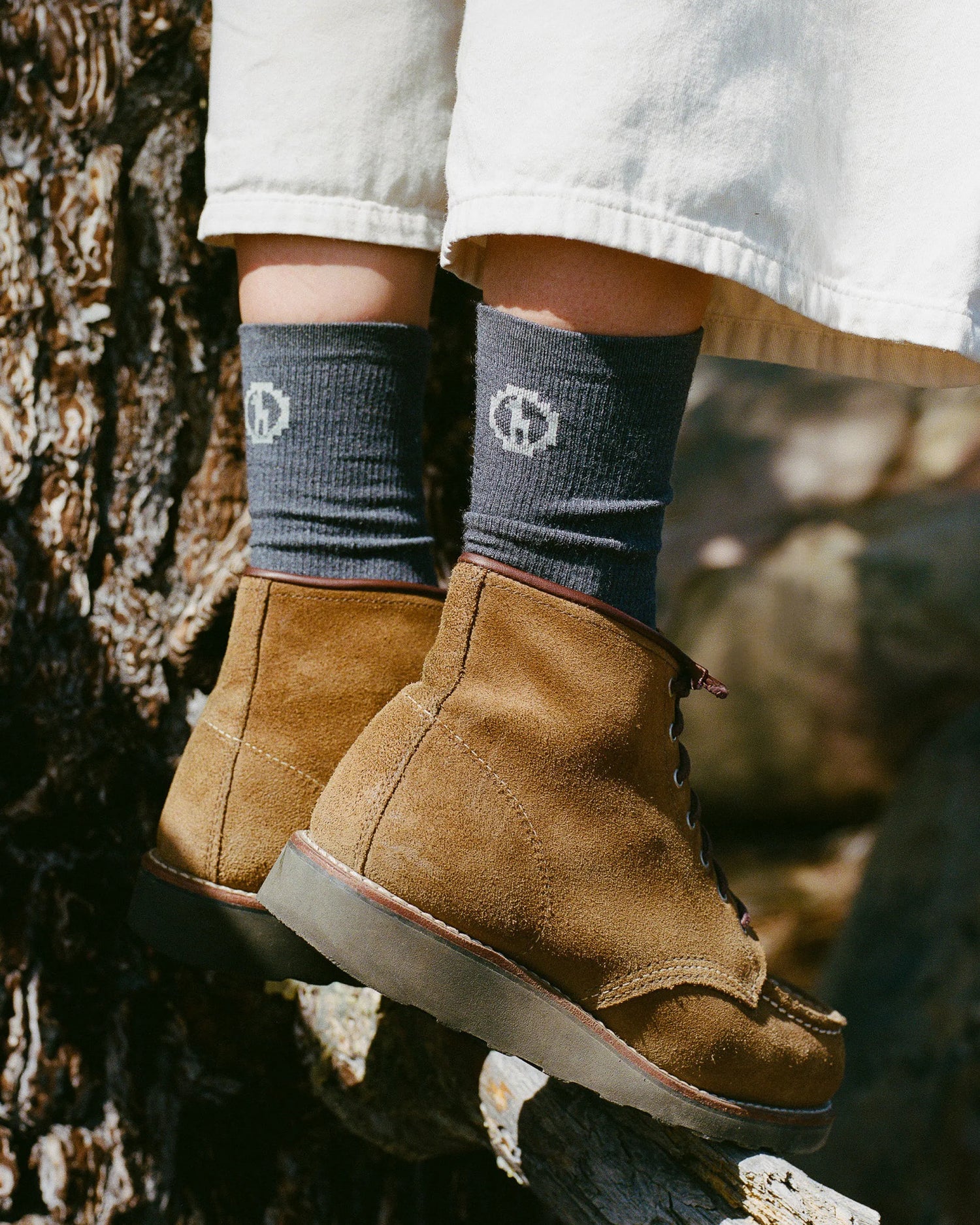 Person wearing brown boots and dark grey socks with a logo, standing on a natural background.