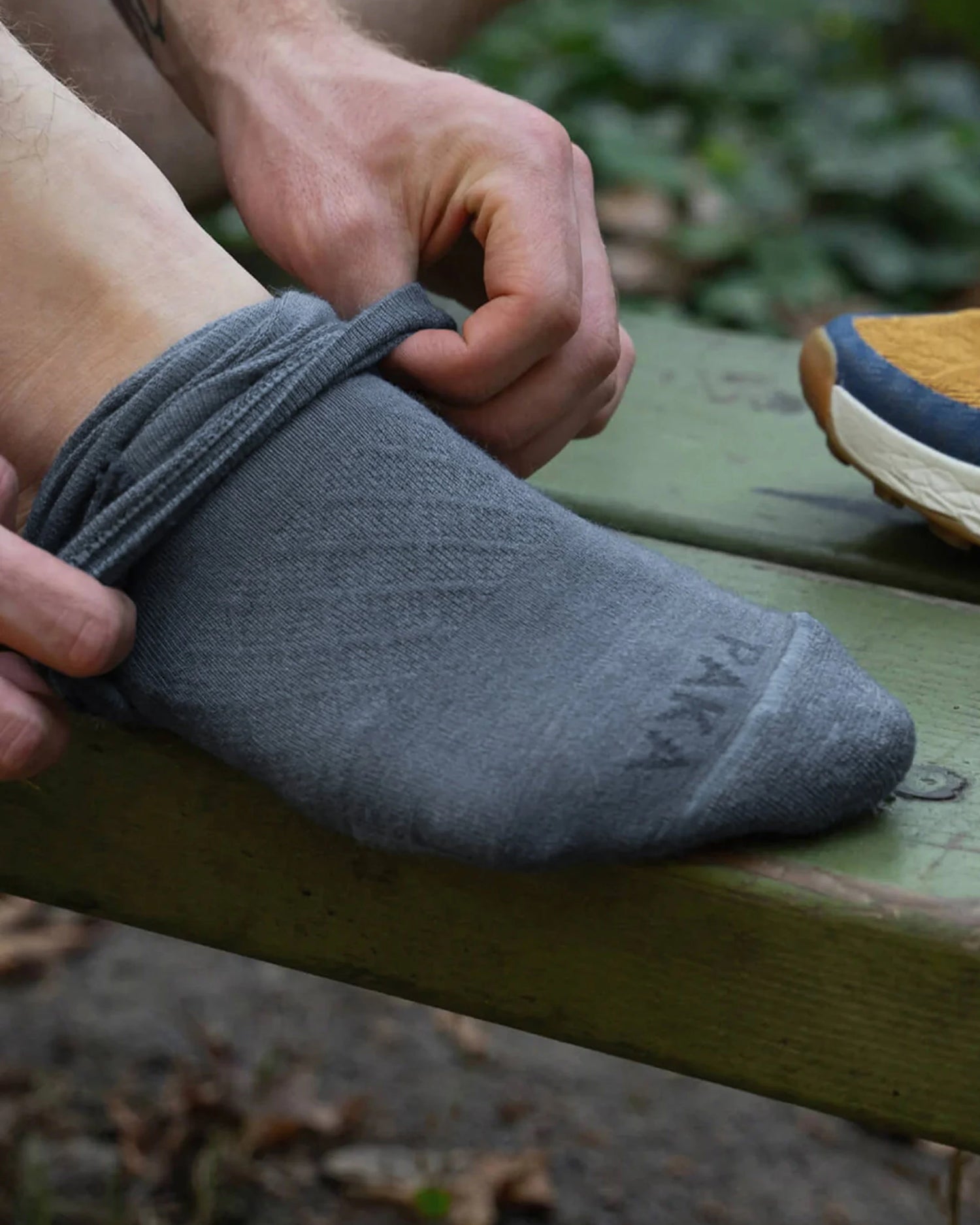 Person putting on an Indigo sock with 'Paka' branding, outdoors.