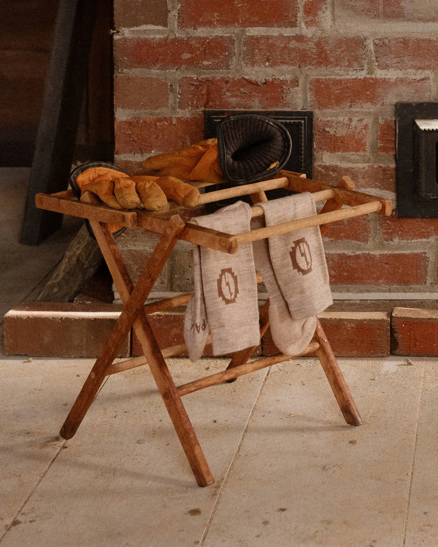 Wooden shoe rack with shoes and towels against a brick wall.