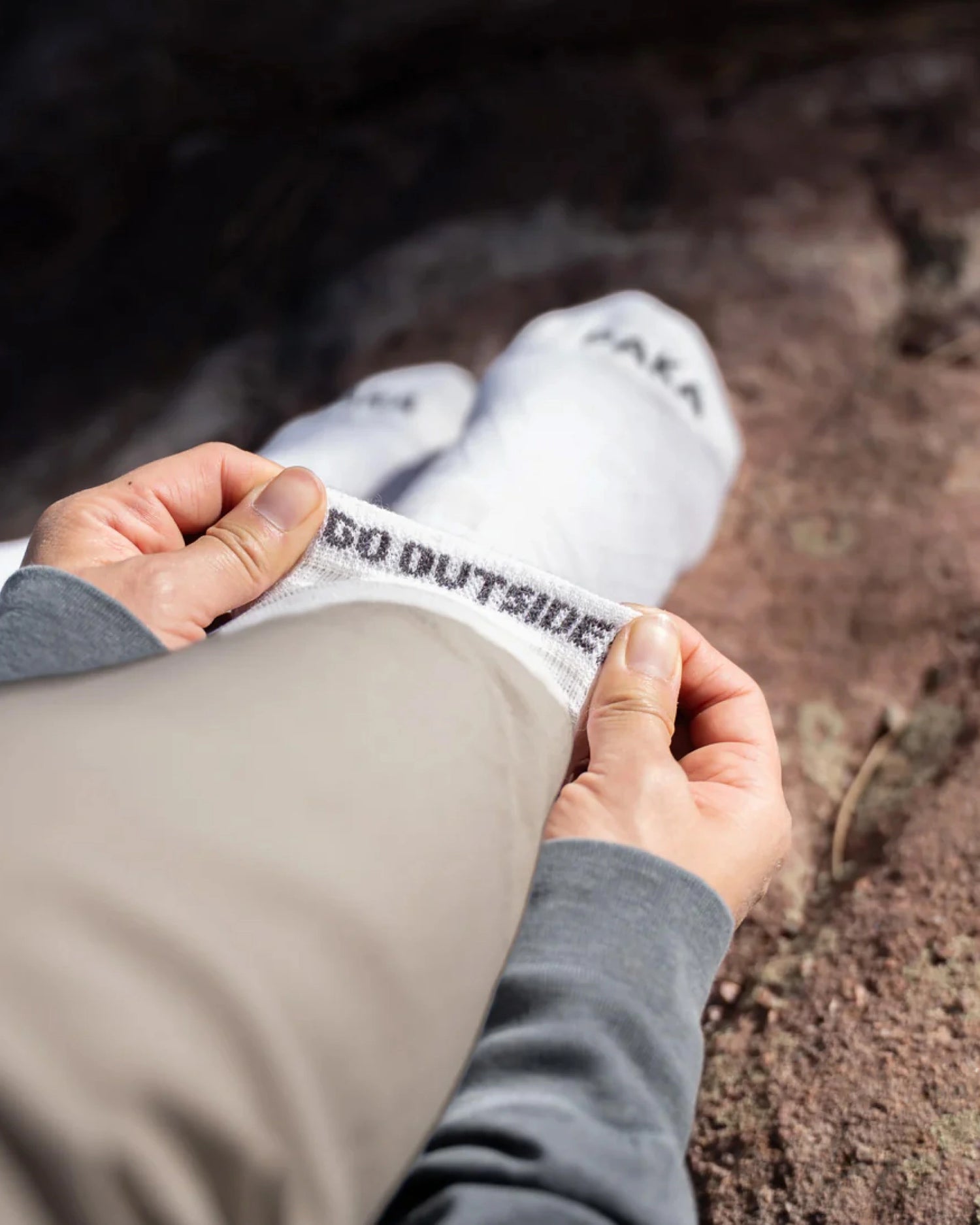 Person holding top of sock rolled over to read 'Go Outside' branded on the inside of the sock with a natural background