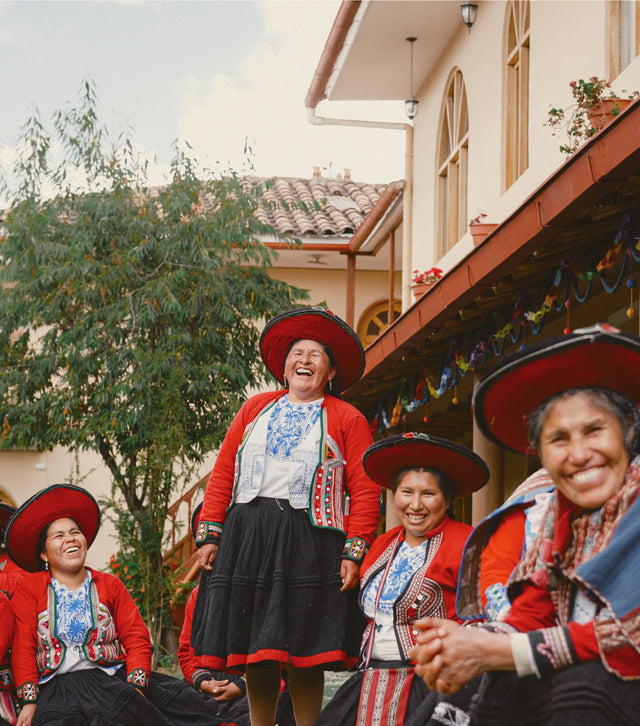 Group of women in traditional red and white woven clothing smiling outdoors in front of a building