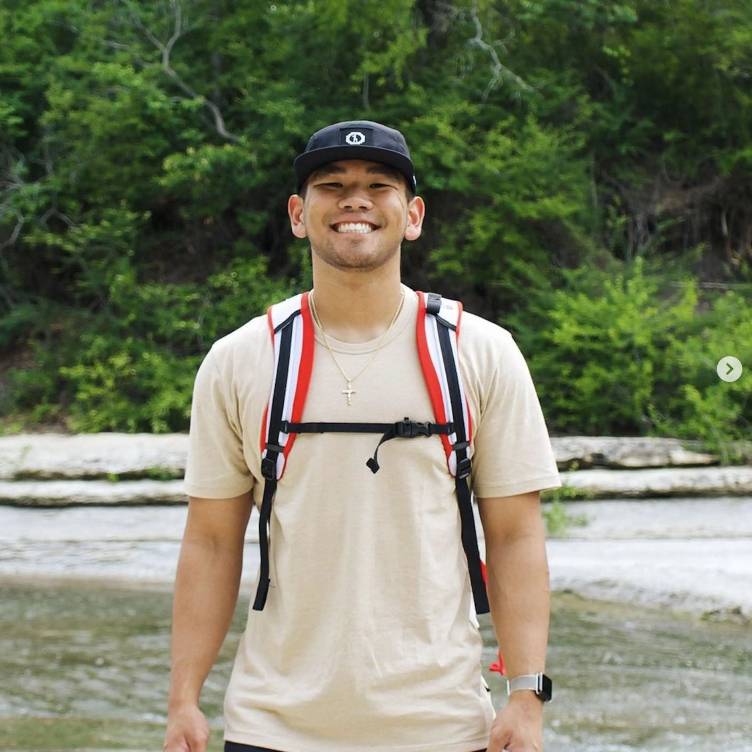 A smiling man wearing a sandstone alpaca tee by a river