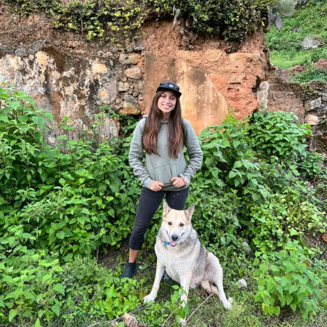 A smiling woman wearing Paka's hat and her dog outdoors