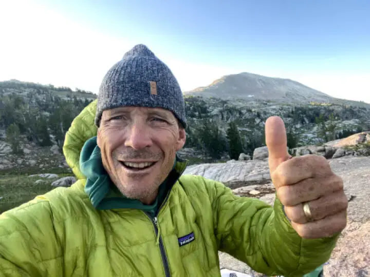 A man with his thumb up in the mountains in his alpaca beanie