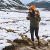 A woman hiking in the snow wearing a green Breathe Full Zip and alpaca socks