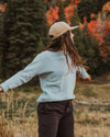 Girl wearing blue crewneck sweater in front of trees