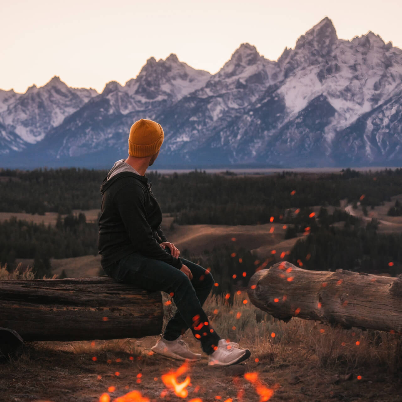 Man wearing alpaca hoodie with bonfire and mountains 