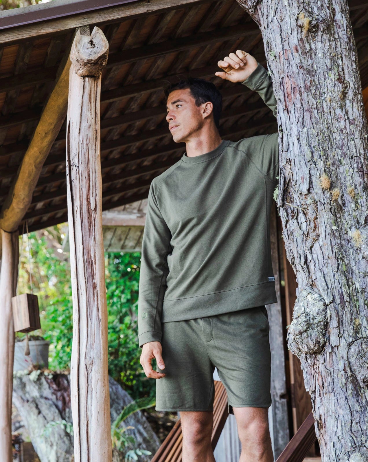 A guy standing in front of a wooden house, wearing our alpaca Terry garments in green
