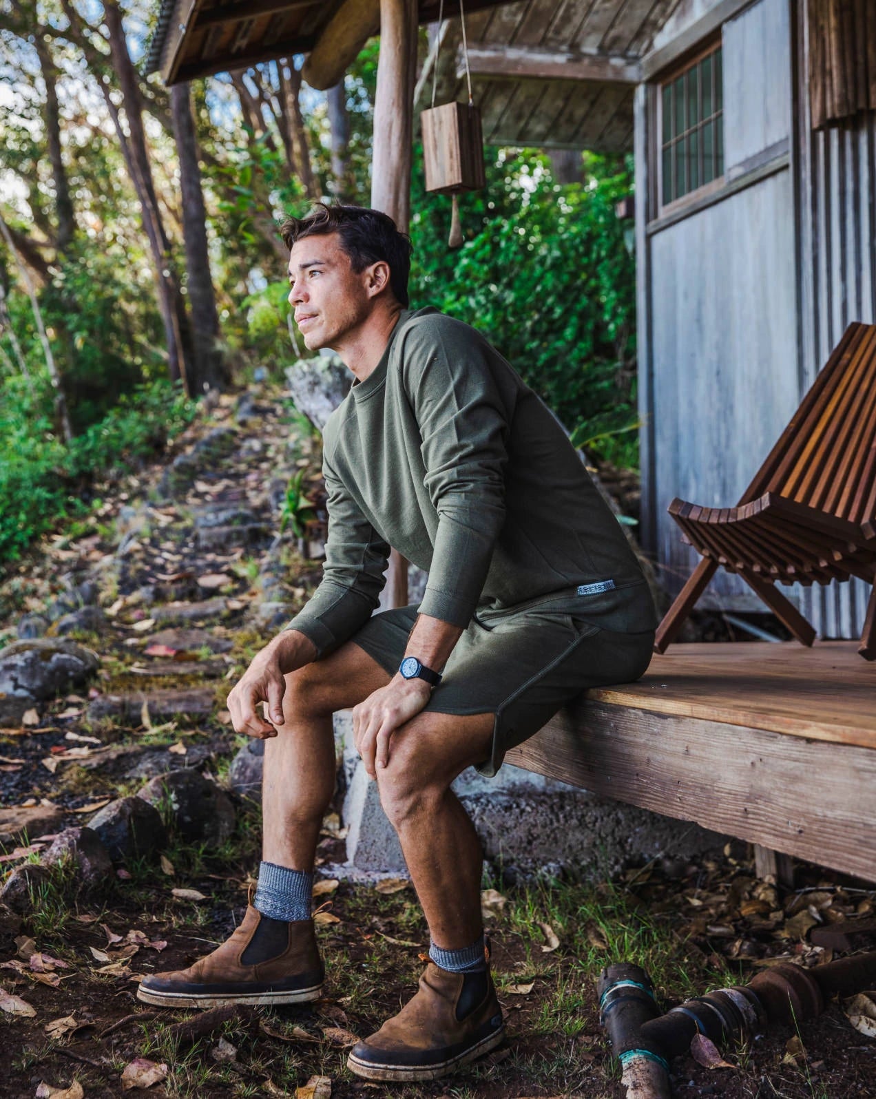 A guy standing in front of a wooden house, wearing our alpaca Terry garments in green