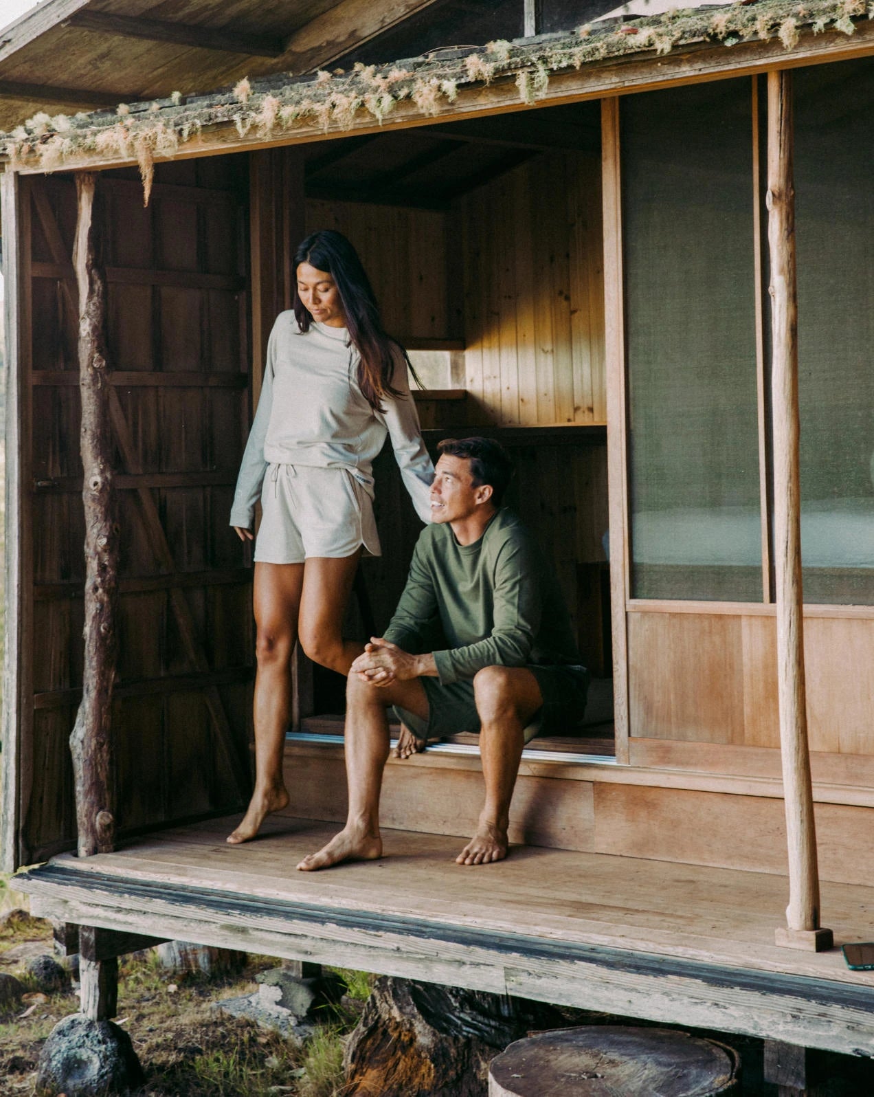 A couple sitting in front of a wooden house, wearing our alpaca Terry garments 