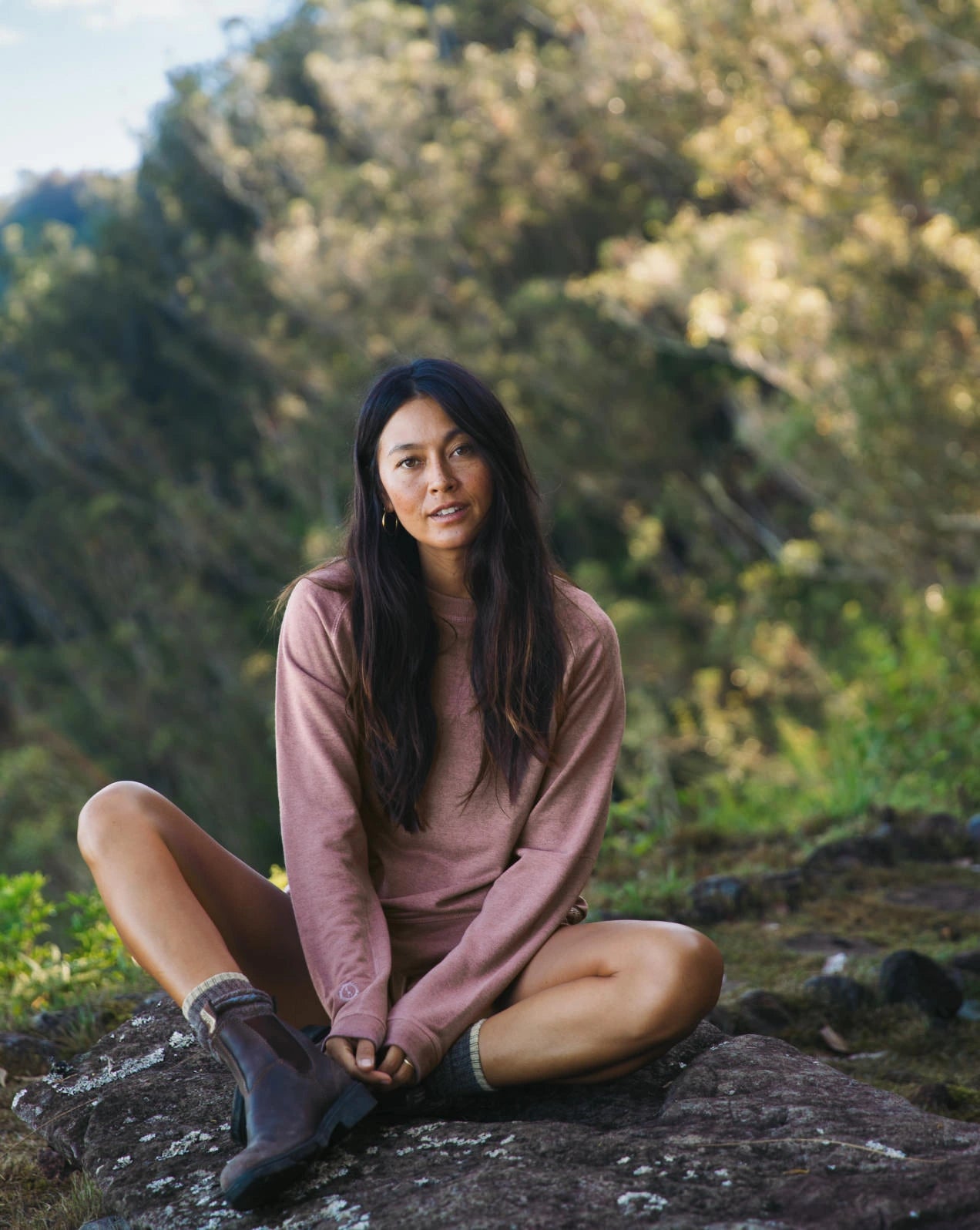 A woman sitting on a rock, wearing our alpaca Terry garments in Iron Oxide outdoors
