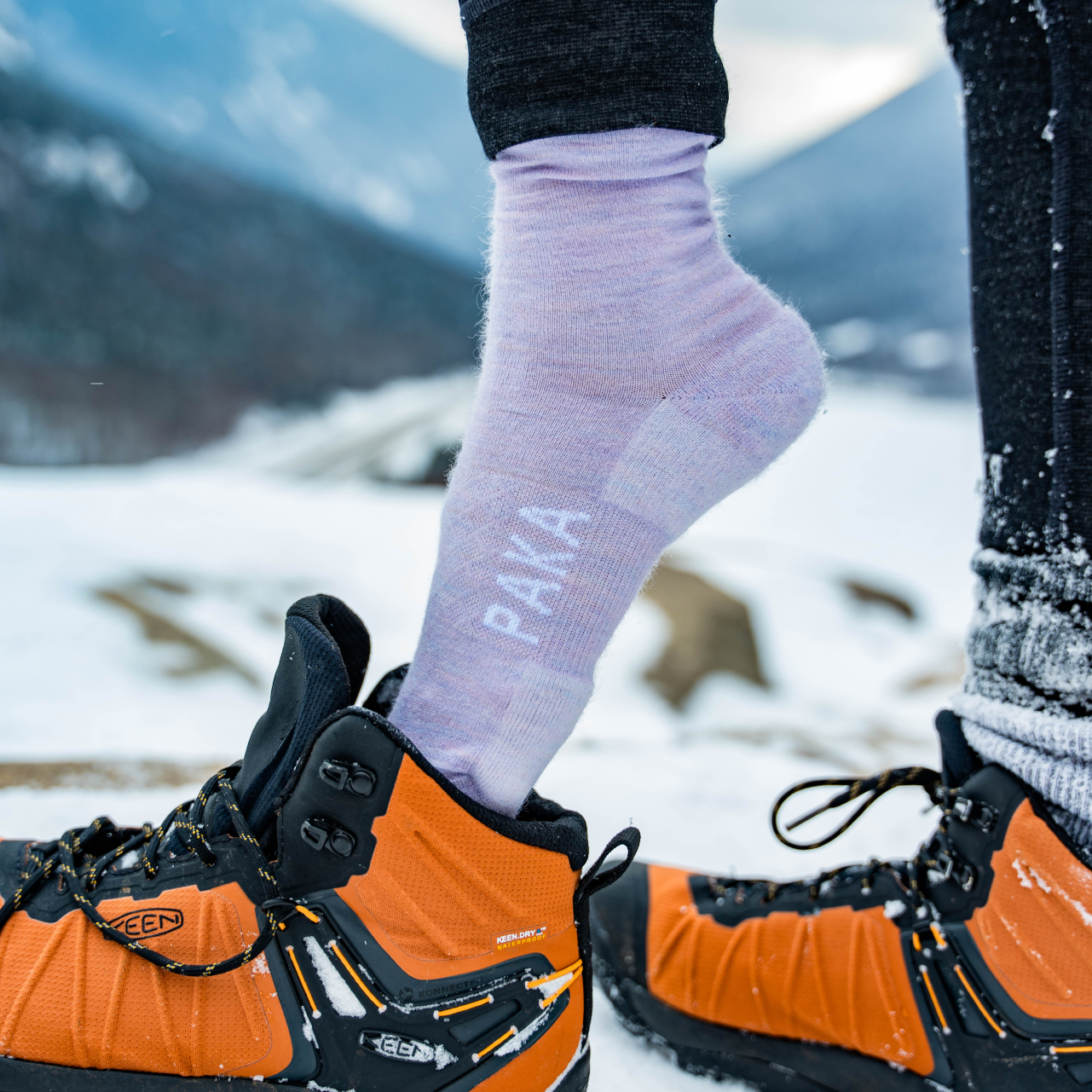 Someone putting on their shoes wearing our lavender alpaca socks in a snowy place