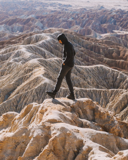 A man wearing an alpaca hoodie walking over the mountains