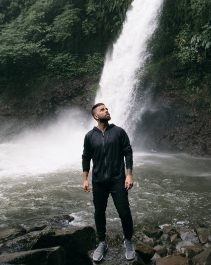 Man wearing our black Breathe Men's Full Zip and joggers in front of a waterfall