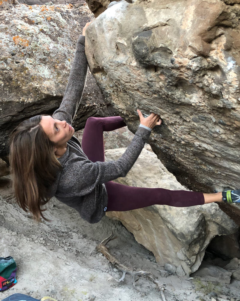 A woman climbing rocks on her Vida hoodie