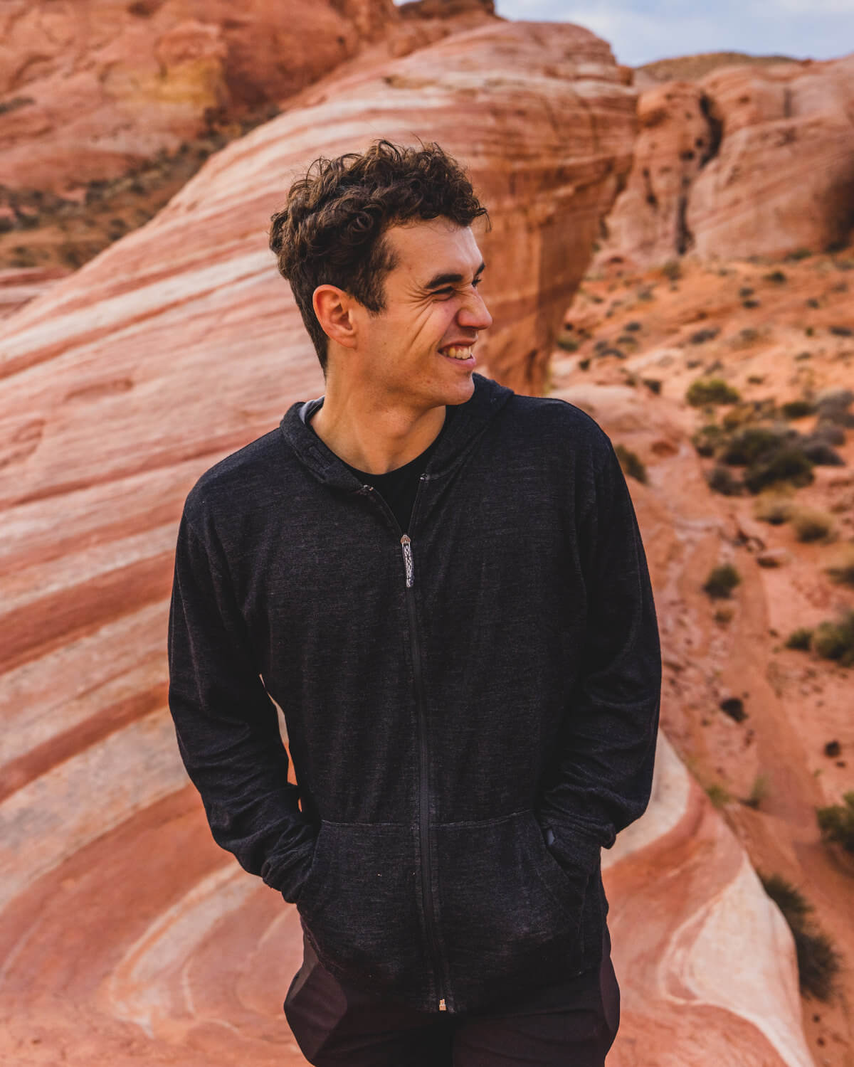 A smiling man wearing a black Breathe Men's Hoodie in a canyon
