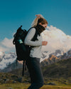 Woman in front of mountains wearing backpack and wearing alpaca base layer 