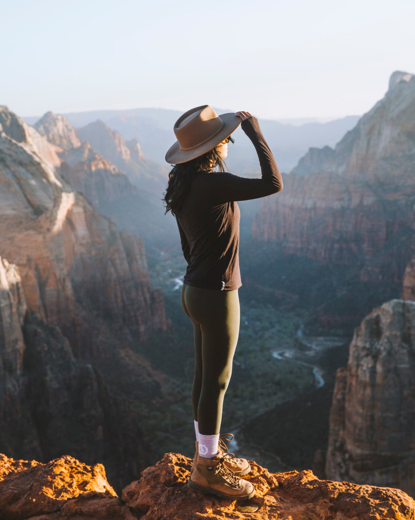 A woman wearing a hat and a clay baselayer looking at a canyon