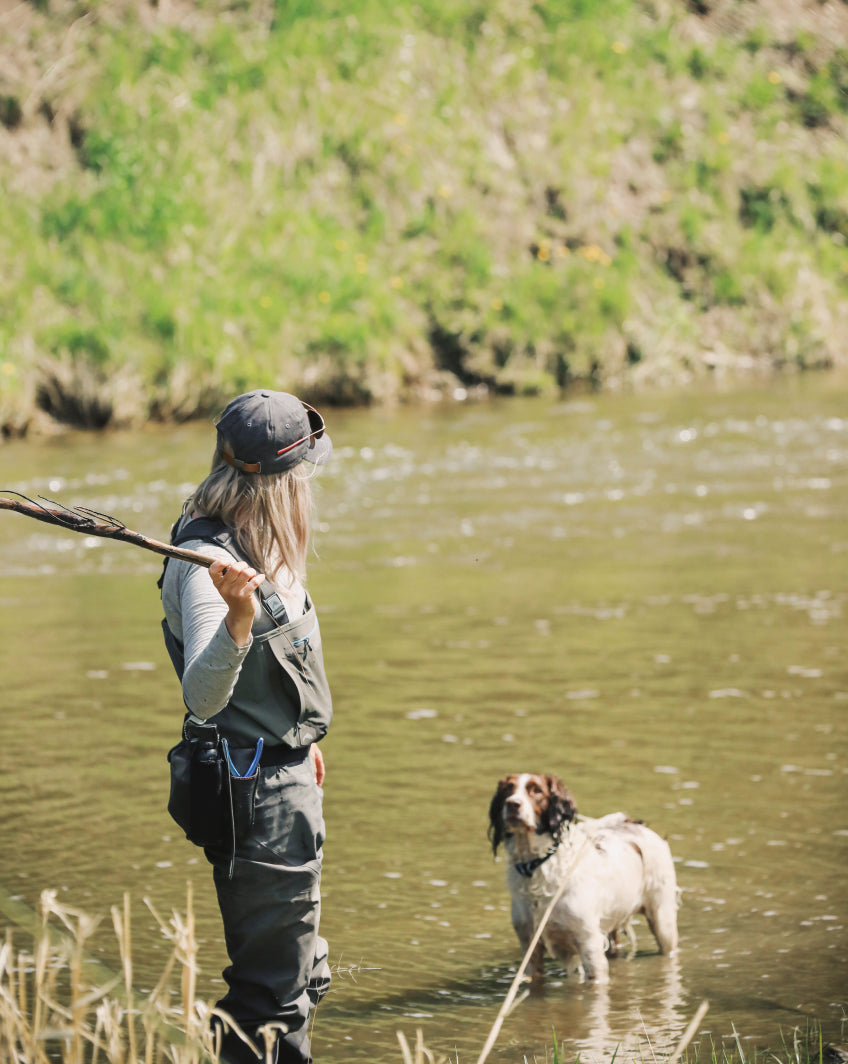 A woman and her dog fishing in a river 