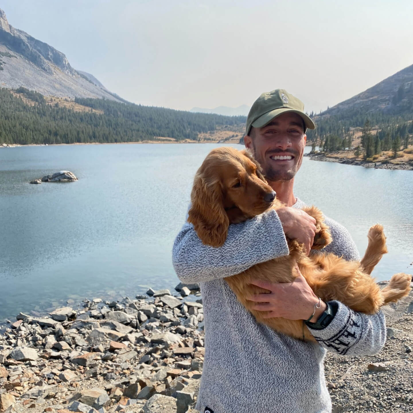 A man holding his dog in front of a beautiful lake