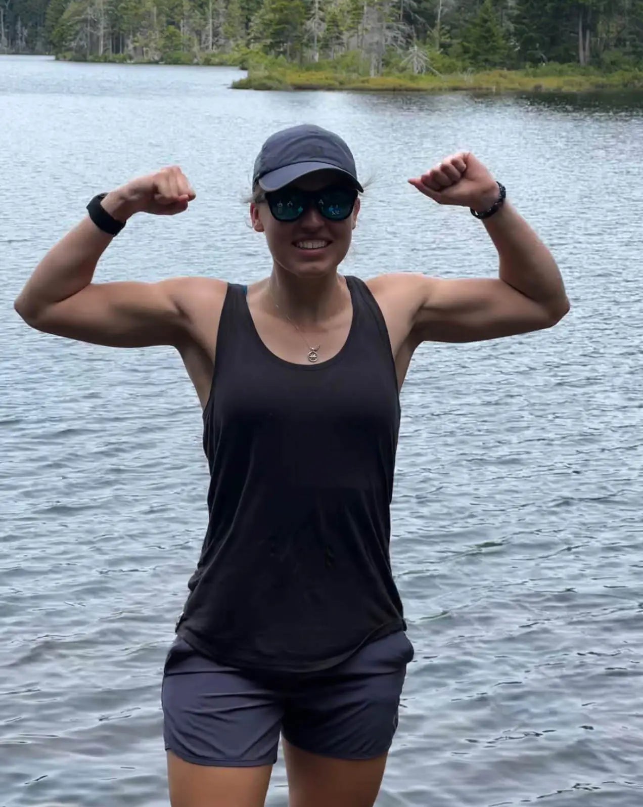 A woman wearing a black alpaca racer tank in front of a lake