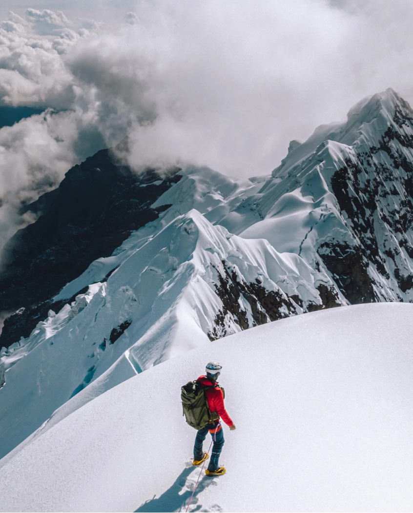 Climber in a red jacket standing in the snow at the top of a mountain 